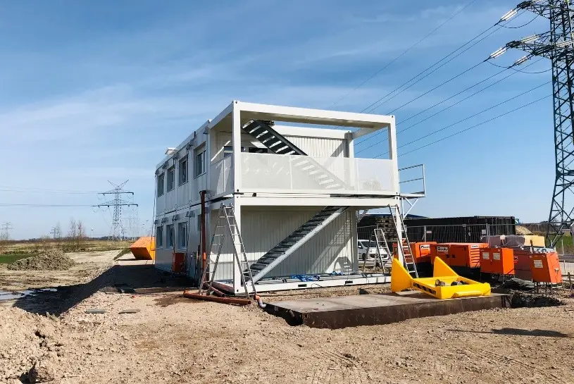 Aufeinander gestapelte Bürocontainer mit einer offenen Treppenansicht an der Seite auf einer Baustelle.