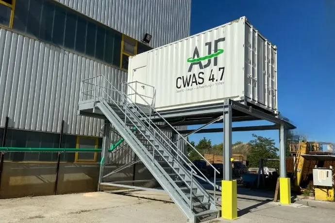 Die Außenansicht eines Containers zur Zement-Wasser-Aufbereitung der CHS Container Group auf einer erhöhten Plattform zu der eine Treppe hinaufführt. 
