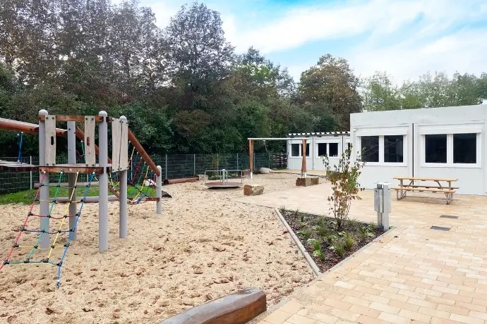 Ein Spielplatz einer Schule der CHS Container Group. Auf der linken Seite sieht man die weißen Container der Anlage.