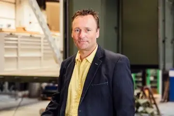 Eine männliche Person, die vor einem Container steht und in die Kamera lächelt, Tony Gutmann