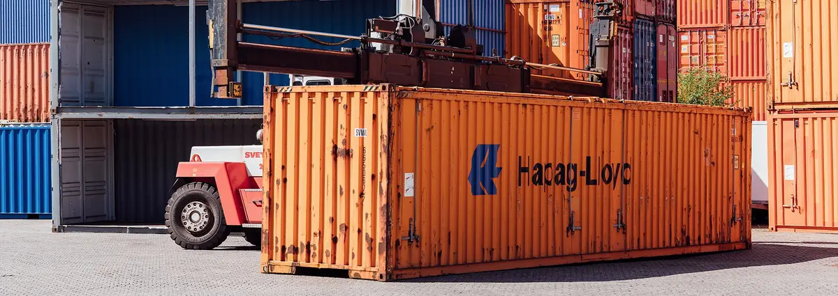 Ein orangener Container steht auf dem Containerdepot der CHS Container Group und wird von einem Gabelstapler hochgenommen.