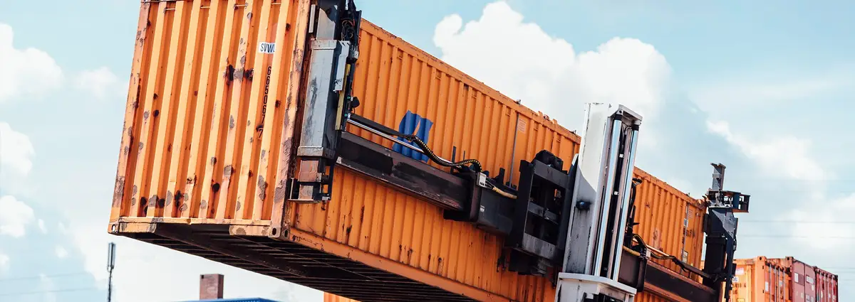 Ein orangener Container befindet sich auf einem Gabelstapler auf einem Containerdepot.