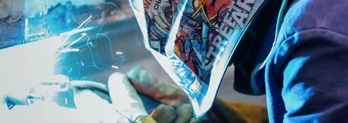 Nahaufnahme einer Schweißermaske und einer Person beim Schweißen. 