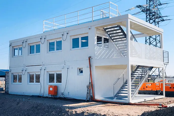 Aufeinander gestapelte Bürocontainer mit einer offenen Treppenansicht an der Seite auf einer Baustelle.