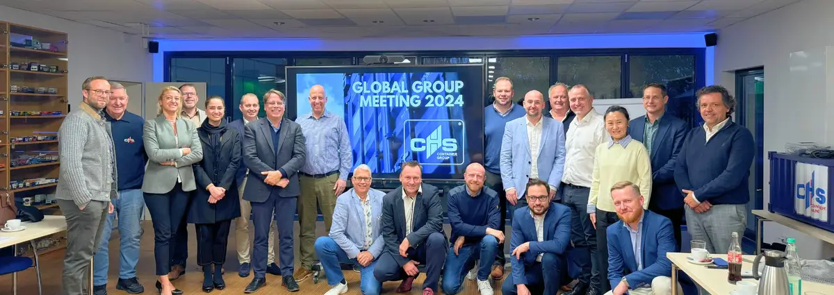 Teilnehmer des Global Group Meetings 2024 stehen im Veranstaltungszentrum vor einem Bildschirm. Auf ihm steht "Global Group Meeting 2024"