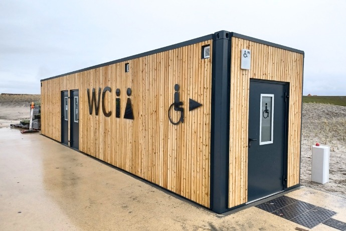 Ein maßgefertigter Sanitärcontainer mit Holzverkleidung im Außenbereich sowie Toiletten für Männer, Frauen und Menschen mit Behinderung.