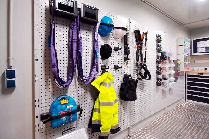 Projekt Werkstatt-Showroom (2) Die Innenansicht eines Werkstatt-Showroom-Containers der CHS Container Group. Man sieht verschiedene Werkstattzubehöre und Schutzkleidung an einer großen Lochwand angebracht.
