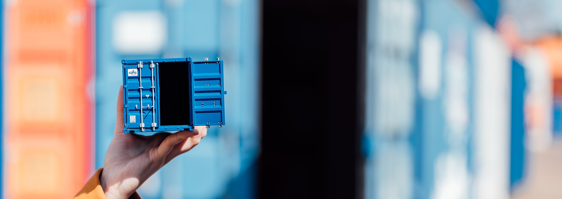 Eine Hand, die einen blauen Miniaturcontainer der CHS Container Group in der Hand hält. Der Hintergrund ist verschwommen.