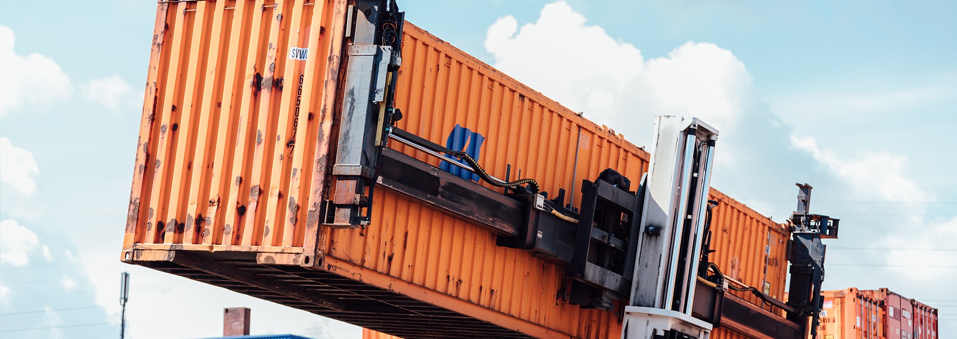 Ein orangener Container befindet sich auf einem Gabelstapler auf einem Containerdepot.