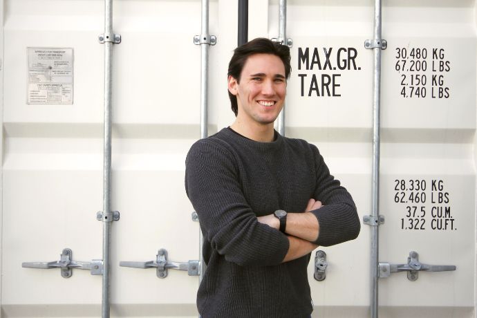 Eine männliche Person steht vor einem Container und lächelt in die Kamera, Daniel 