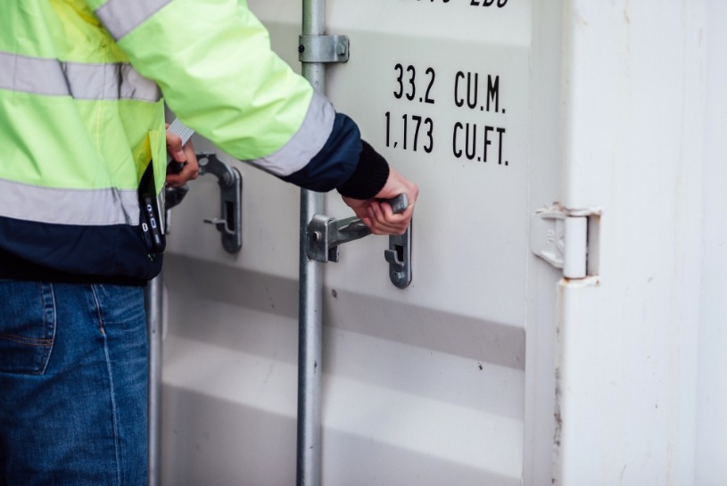 Headert Containerschlösser Eine Person, die einen weißen Container öffnet. Der Fokus liegt auf den Händen.