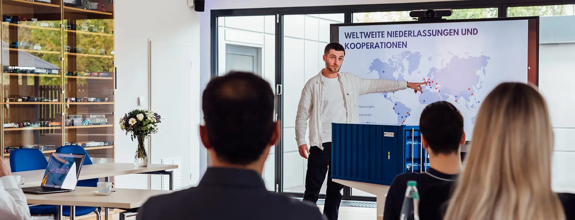 Startseite-Titelbild-CHS-Containerschulung Person steht vor einem großen Bildschirm und zeigt auf einer Karte die verschiedenen Standpunkte der CHS Container Group