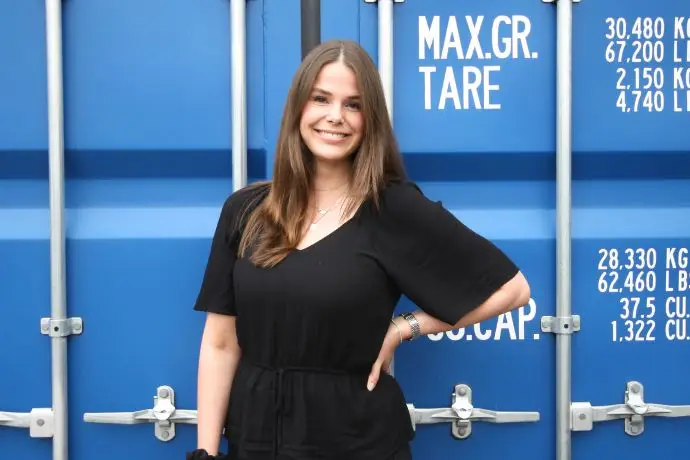 Eine weibliche Person, die vor einem Container steht und in die Kamera lächelt, Nina Bleeker