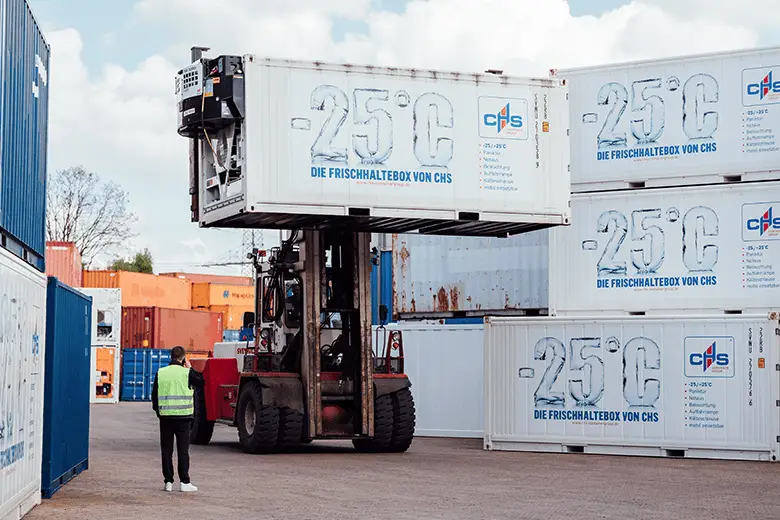 Un contenedor refrigerado siendo transportado por una carretilla elevadora a través de una terminal de contenedores.