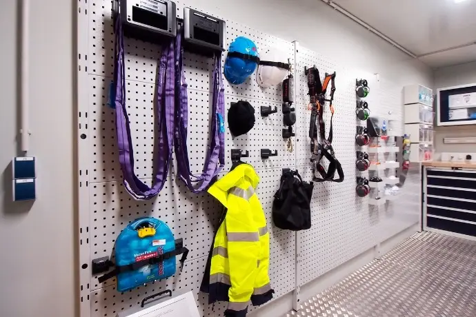 Projekt Werkstatt-Showroom (2) Die Innenansicht eines Werkstatt-Showroom-Containers der CHS Container Group. Man sieht verschiedene Werkstattzubehöre und Schutzkleidung an einer großen Lochwand angebracht.