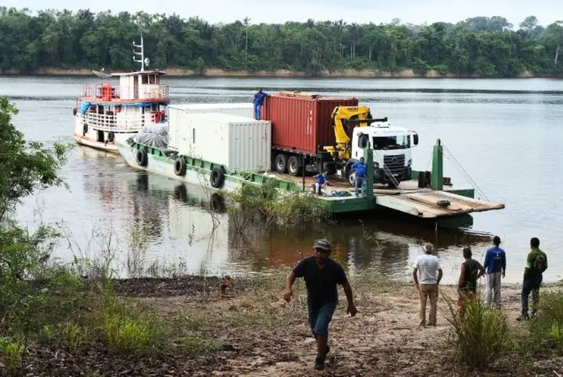 Mehrere Container und LKWs auf einem großen Boot, dass von einer Seite des Flusses zur anderen fährt.