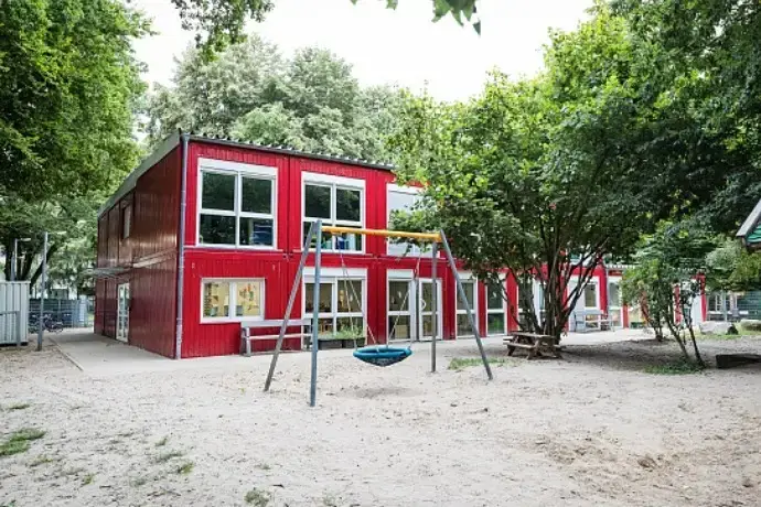 Eine rote Containeranlage der CHS Container Group, die als Schule verwendet wird. Im Vordergrund sieht man einen Spielplatz.