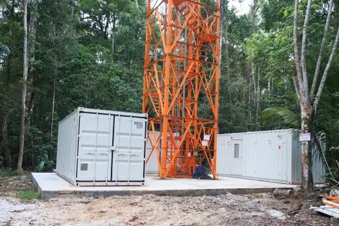 Zwei weiße Container der CHS Container Group, die in einem Regenwald stehen. In der Mitte befindet sich ein großer Mast zur Klimaforschung.