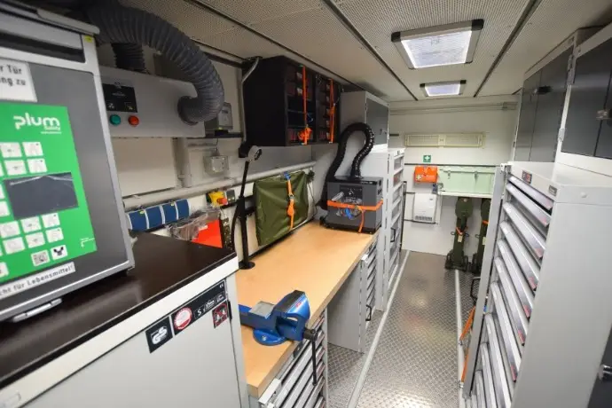 Projekt PzH (1) Die Innenansicht eines Werkstattcontainers für militärische Anwendungen der CHS Container Group. Man sieht verschiedene Werkbänke und Schränke mit Werkzeugen.