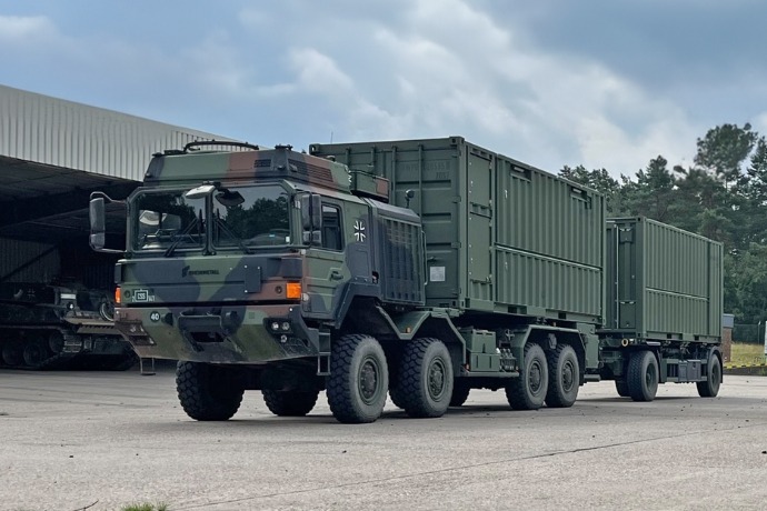 Ein Werkstattcontainer für die militärische Anwendung der CHS Container Group. Der Container hat ein Tarnmuster und ist hinten geöffnet. Eine Treppe hinten und in der Mitte des Containers führt nach oben in den Container.