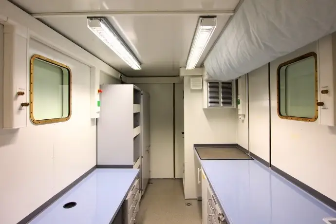 Die Innenansicht eines Schiffslabor der CHS Container Group. Man sieht mehrere Tische, Regal und zwei Fenster an den Seiten des Containers.