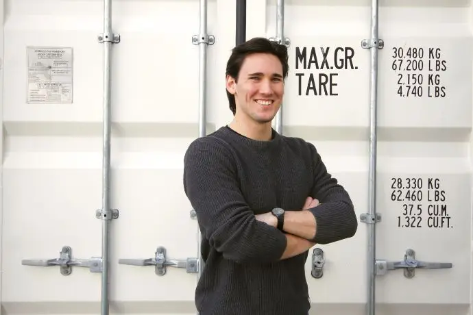 Berufsportrait Daniel Eine männliche Person steht vor einem Container und lächelt in die Kamera, Daniel