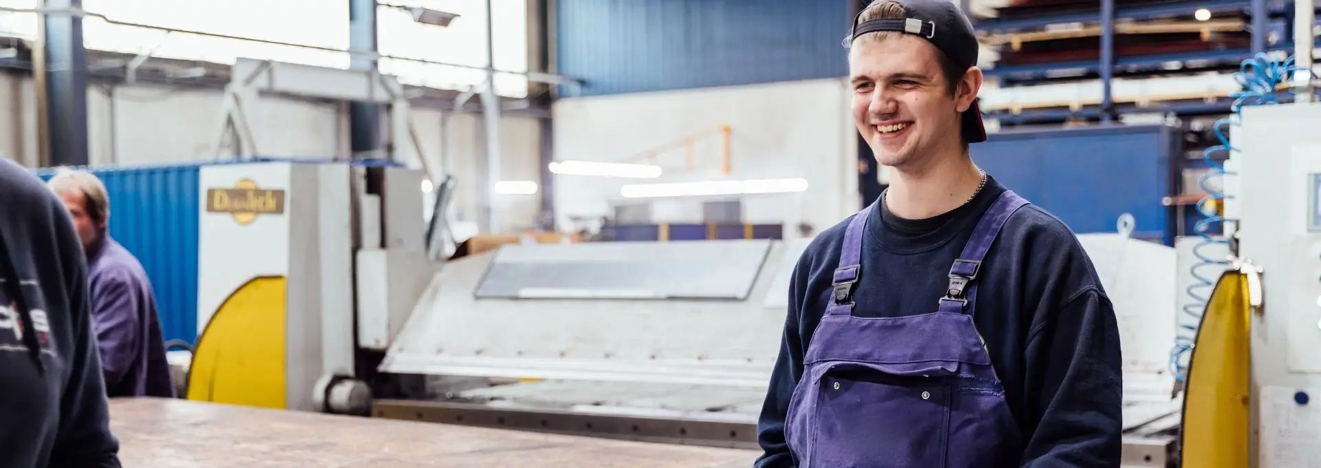 Design ohne Titel (64) Eine männliche Person trägt eine graue Platte in einer Werkstatt für Container. Er lächelt dabei.