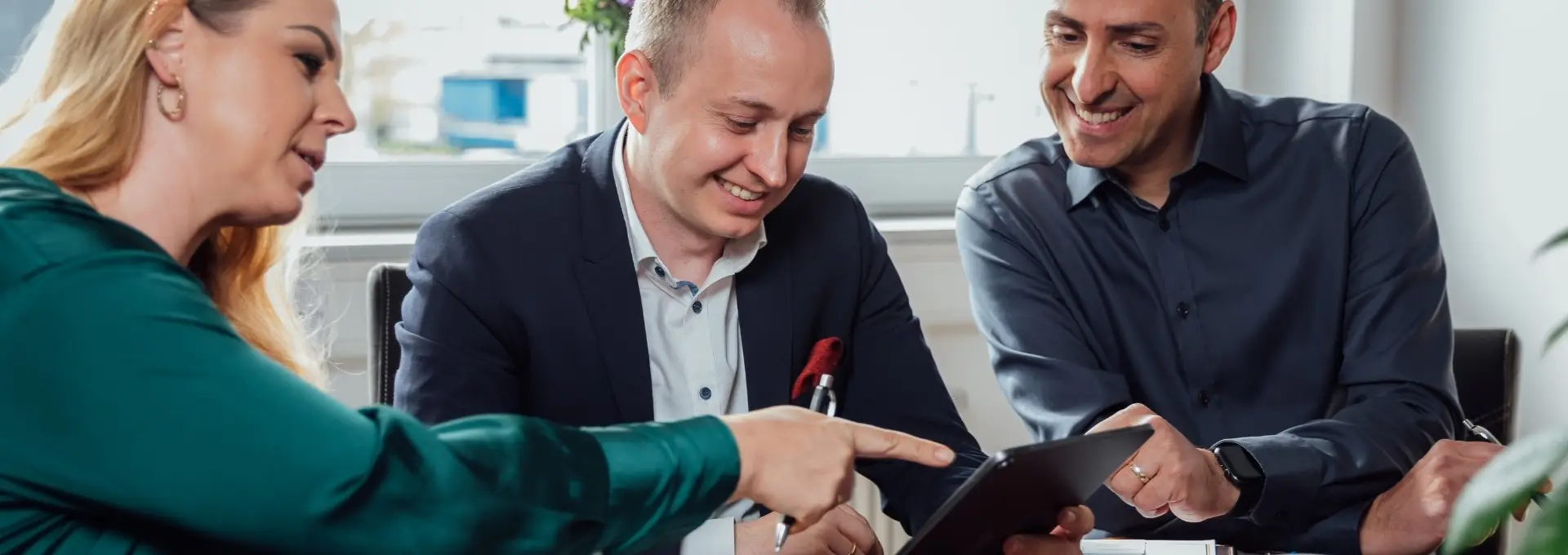 Zertifikate Header Desktop Drei Personen schauen gemeinsam auf ein Tablet. Sie befinden sich in einem Meeting und vor ihnen steht Kaffee und Kekse auf dem Tisch.